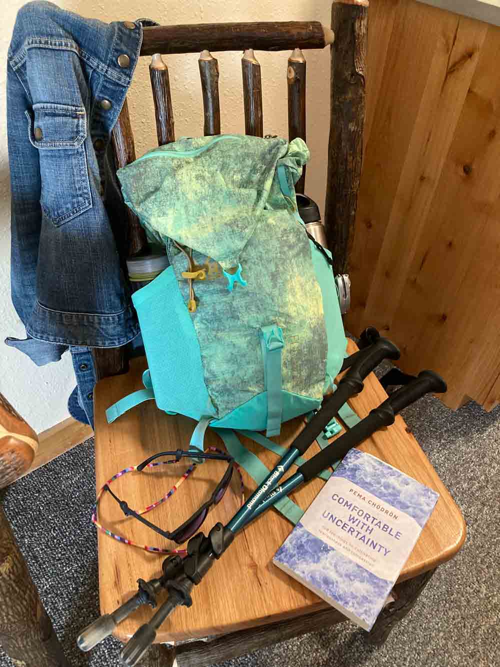 Backpack, hiking poles, glasses, book, jean jacket on chair